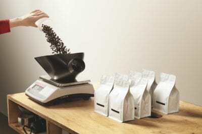 hand pours roasted coffee on weight before package bag e1625191261981 hand-pours-roasted-coffee-on-weight-before-package-bag-e1625191261981